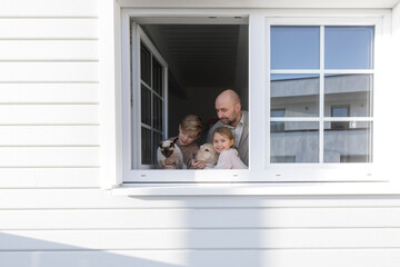 Father with his two children, dog and cat at opened window of their house