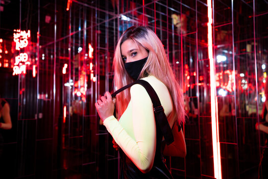 Young woman wearing protective face mask standing in red light room