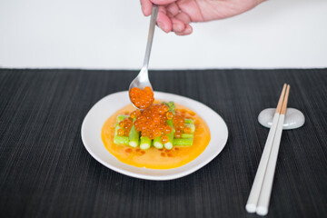 Hand puts red salmon caviar on Mini asparagus with sauce on white plate in Japanese restaurant, close up, flat lay, picture for the menu, healthy food
