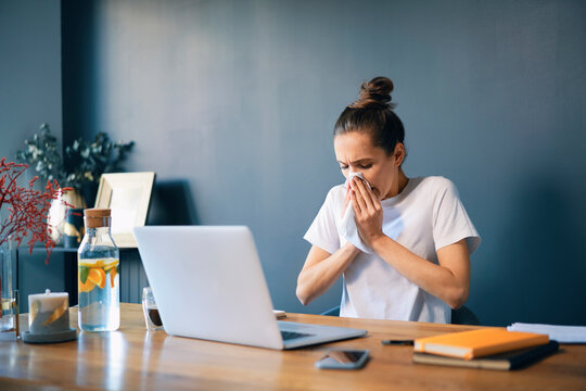 Businesswoman blowing nose while sitting at desk in home office