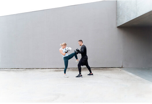 Woman practicing kickboxing with man while standing against wall
