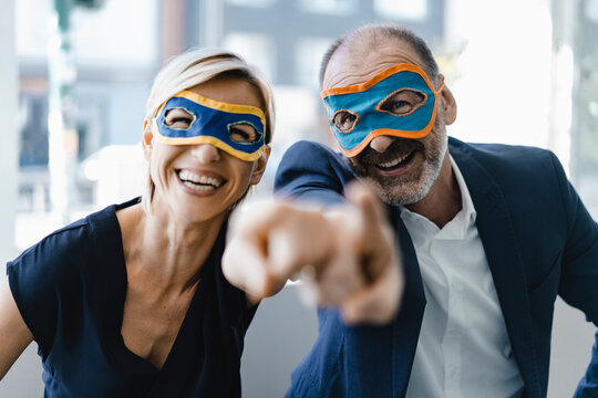 Businessman and woman wearing super hero masks, pointing at camera