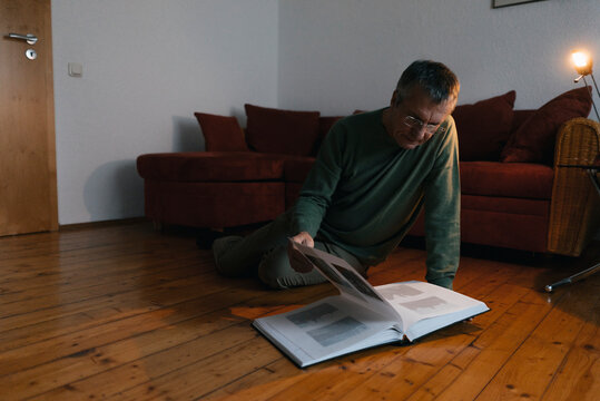 Senior man sitting on the floor at home looking at photo album