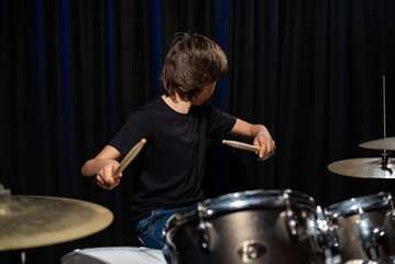 The boy learns to play the drums in the studio on a black background. Music school student