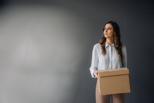 Serious young businesswoman holding cardboard box