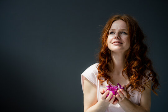 Portrait of redheaded woman with hadful of purple orchid blossoms
