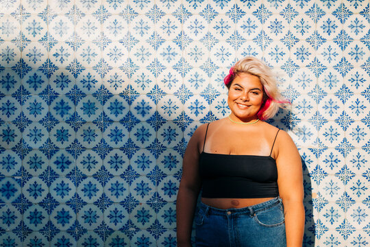 Smiling young woman standing against patterned wall