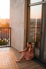 Portrait of a schoolgirl girl in a beautiful pink dress with long hair on a large terrace in the setting sun
