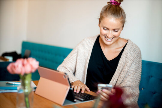 Portrait of happy young woman at home office looking at smartphone