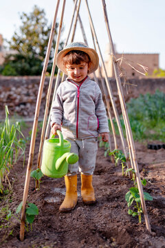 Smiling cute girl holding watering can standing under trellis at orchard