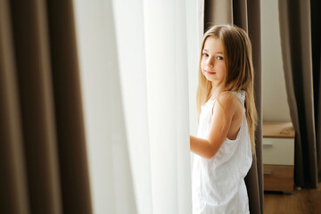 Naklejka premium Little girl with long hair by the window