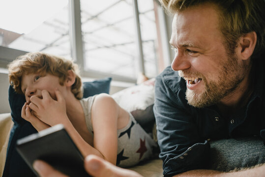 Father and son lying on couch having fun with cell phone