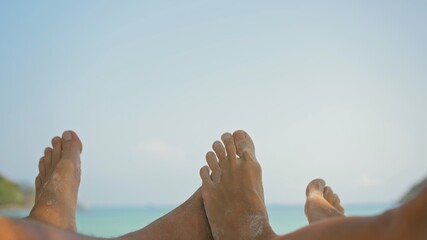Bare feet of young man and woman couple wiggle lying on beach near calm azure ocean at exotic...