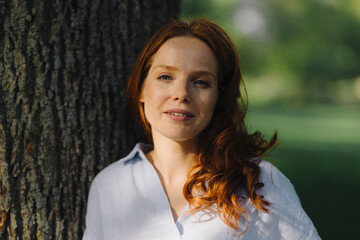 Portrait of redheaded woman at tree in a park