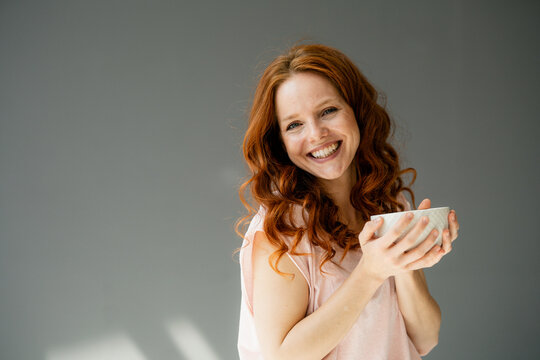 Portrait of happy redheaded woman with cereal bowl against grey background