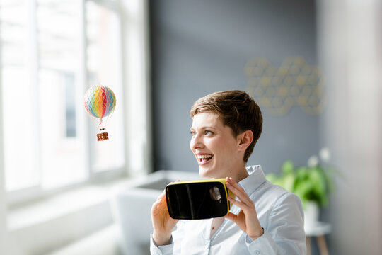 Smiling woman with VR glasses and small hot-air balloon in office