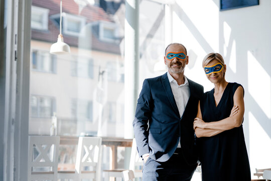 Businessman and woman wearing super hero masks, standing in coffee shop
