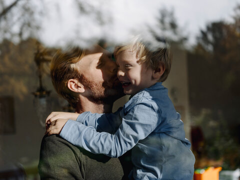 Father carrying and kissing son at the window at home