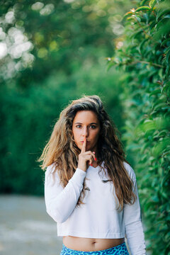 Young woman with finger on lips standing by plants in park