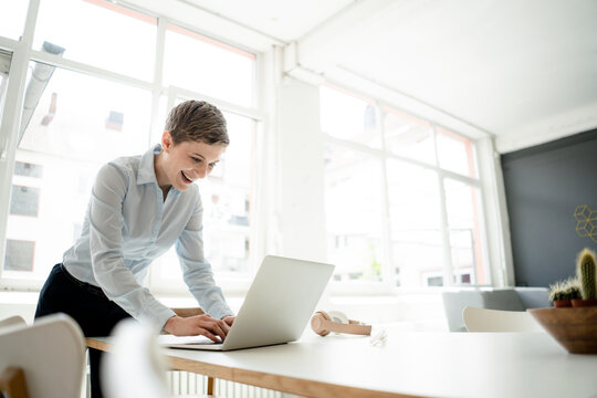 Happy businesswoman using laptop on table in office