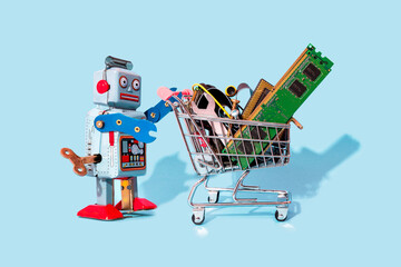 Studio shot of vintage robot toy pushing miniature shopping cart filled with electronic equipment