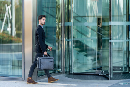 Young businessman carrying briefcase while walking toward office building