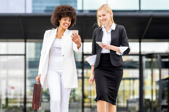 Business People Using Mobile Phone While Walking Against Building