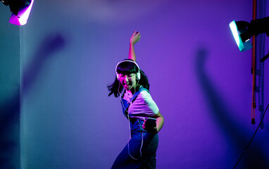 Cheerful woman singing and dancing while listening music through headphones against backdrop