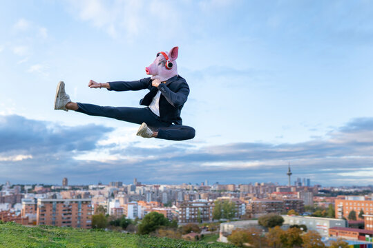 Male entrepreneur wearing pig mask practicing kickboxing while jumping against sky
