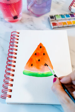 Woman painting watermelon slice with watercolor in book