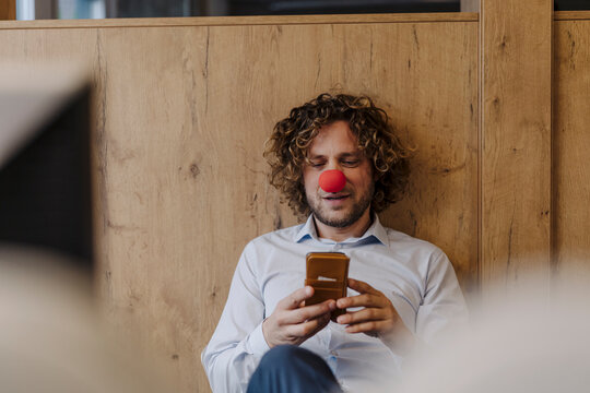 Businessman with red clown nose using cell phone in office