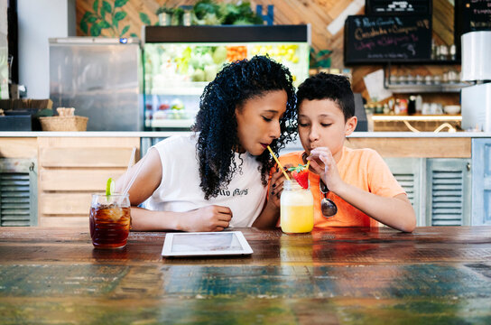 Boy sharing smoothie with mother while sitting at table in restaurant