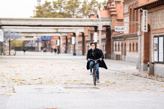Young man cycling on street with autumn leaves in city during pandemic