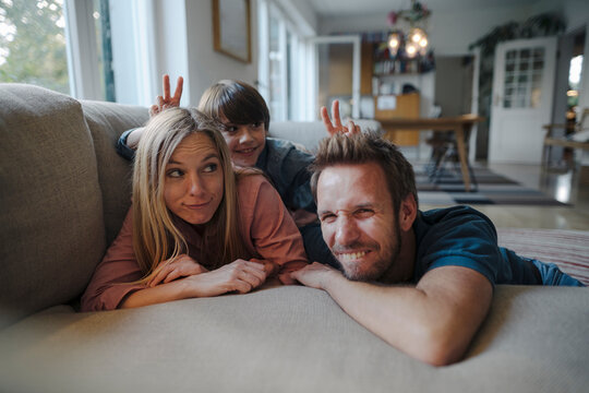 Happy family lying on couch, son making fun of his parents