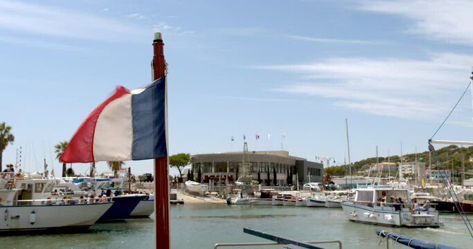 French flag flying on a boat docking pier in small town in France. People gathering on boats during summer