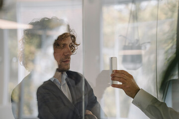 Businessman showing cell phone to colleague behind glass pane