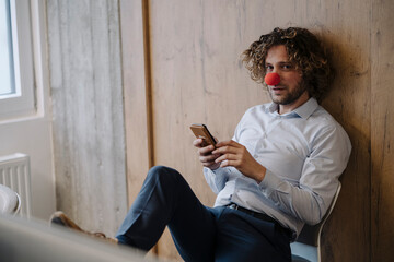 Portrait of businessman with red clown nose using cell phone in office