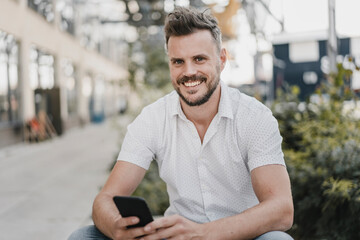 Young smiling man using smartphone and looking at camera