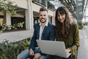Portait of smiling businessman and casual businesswoman using laptop outdoors