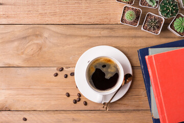 Coffee cup with cactus and book on the wooden background with copy space, top view