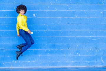 Happy fashionable woman with smart phone jumping against blue wall