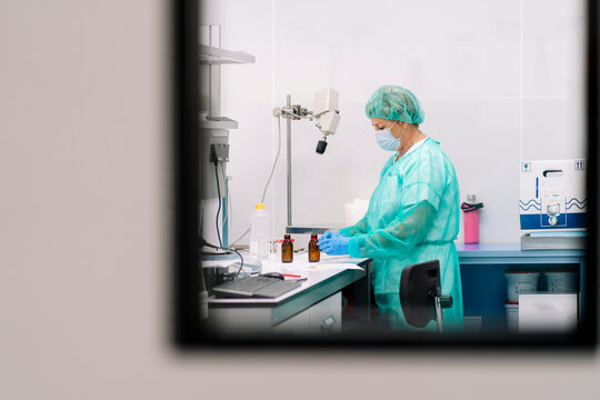 Female scientist working at table in laboratory seen through window