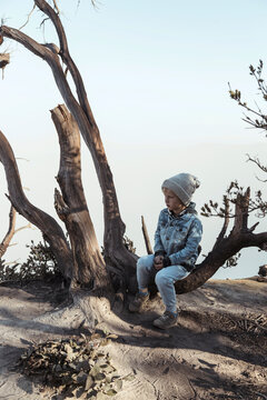 Young boy sitting on a tree at the edge of volcano Ijen, Java, Indonesia