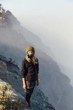Young woman with respirator mask standing at the edge of volcano Ijen, Java, Indonesia