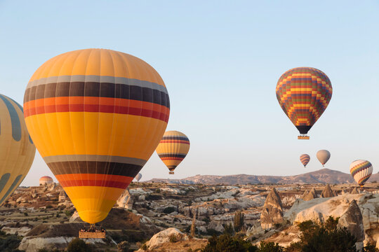 Colorful hot air balloons flying over rocky landscape against clear sky in Cappadocia, Turkey