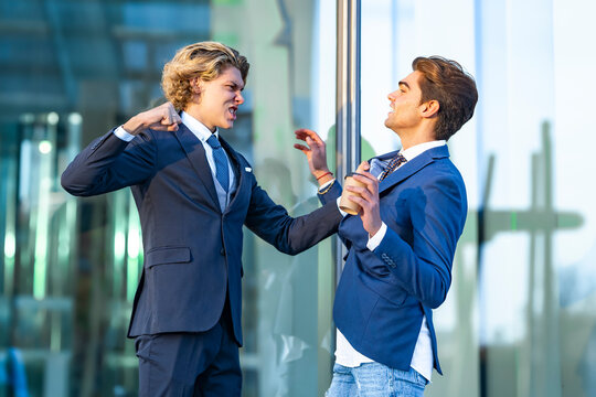 Angry young businessman fighting with male colleague outside office building
