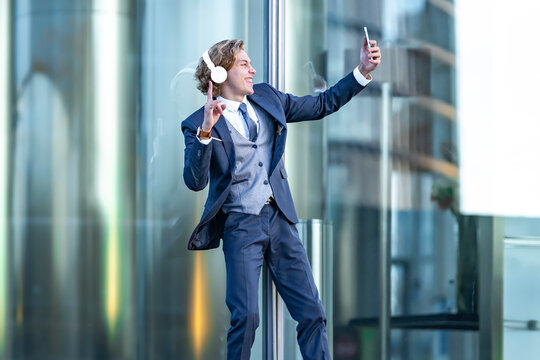Happy male professional gesturing while taking selfie through smart phone against office building