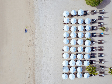 Indonesia, Bali, Aerial view of man sunbathing in front of rows of beach umbrellas on sandy coastal beach of Nusa Dua