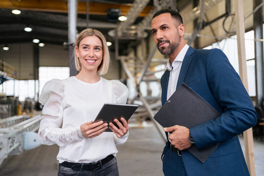 Businessman and smiling young woman with tablet in a factory