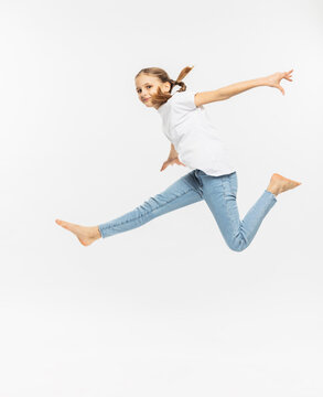 Girl with arms outstretched gesturing while jumping by white background